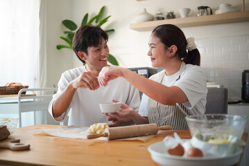 Happy couple baking together in the kitchen, smiling and preparing dough for homemade pastries.