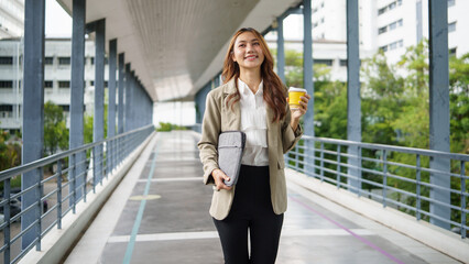 Confident businesswoman holding a yellow coffee cup walking on an outdoor walkway.