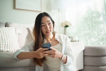 Young Asian woman relaxing indoors and using mobile phone.
