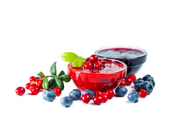 Bowls of blueberry and lingonberry jam with berries and leaves isolated on white background.