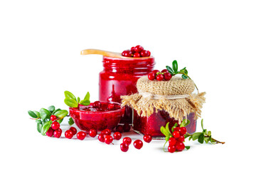 Jar and bowl of lingonberry jam with berries, leaves and wooden spoon isolated on white background.