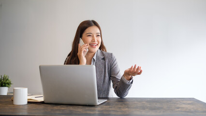 Smiling businesswoman talking on the phone while working on a laptop at a desk.