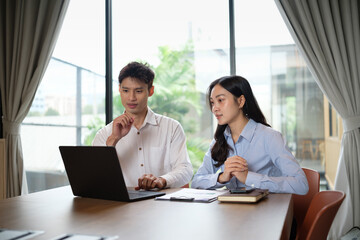 Two young business professionals working together on laptop during meeting in modern office.