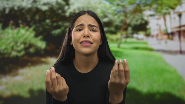 Woman extends hands pleading in park, begging young latin hispanic strangers amid green outdoors setting for assistance.
