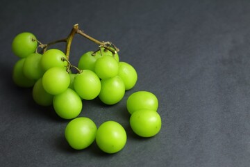 A bunch of fresh and juicy green Shine Muscat grapes neatly arranged with some fruit falling off the stem, placed on a dark background