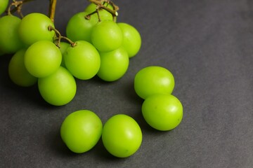 A bunch of fresh and juicy green Shine Muscat grapes neatly arranged with some fruit falling off the stem, placed on a dark background