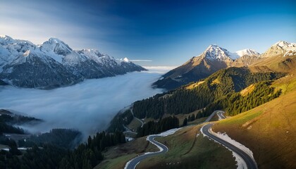 aerial view of winding mountain road through the alps with snow capped peaks and morning fog