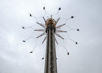 Upward view onto the top of the tower of a modern swing carousel with flying seats against the cloudy sky at Gr&ouml;na Lund amusement park in Stockholm, Sweden;