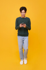 Obraz na płótnie Canvas Smartphone user on yellow background, casual man texting and browsing, full-length portrait with copy space for app promotion, social media, lifestyle marketing, digital communication