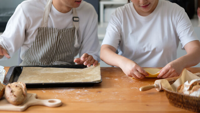 Close-up of hands shaping pastry dough with a baking tray and fresh bread in a homey kitchen setup.