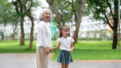 Fototapeta premium Elderly woman and little girl enjoy a serene walk while holding hands in the park.