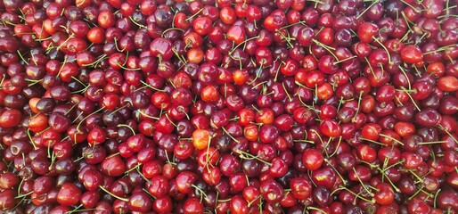A vibrant overhead shot shows a large pile of fresh, ripe cherries. The rich red fruit with their green stems and glossy skin are packed closely together, creating a beautiful and appetizing texture.