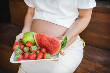 Expectant mother holding a plate with fresh summer fruits