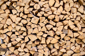 Pile of neatly stacked firewood displays array of shapes and sizes. Bright natural light highlights warm wood tones, creating rustic and cozy atmosphere. Ideal for winter preparation or rustic decor