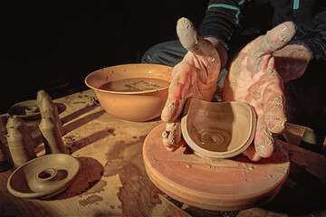 Potter's hands while working on the wheel, top view with dark background. Master makes a pot on a potter's wheel