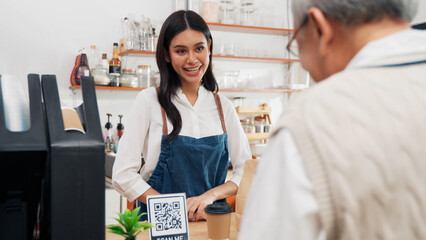 Asian senior male customer is paying for coffee through a mobile phone app to an Asian female barista coffee shop owner