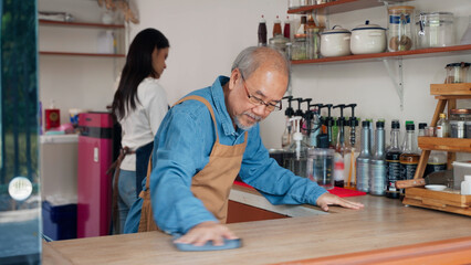 Asian senior owner man of a small coffee shop is cleaning the counter where he sells coffee