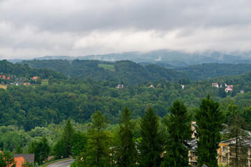 Panorama of the Bieszczady Mountains with green hills, forests, and houses among trees under clouds. © Adam