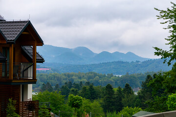 View of Bieszczady mountains from wooden house terrace, with green forests and mist-covered mountain peaks in the background.