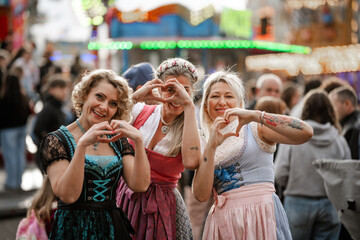 Fototapeta premium Three women celebrate Bavarian heritage in dirndl costumes at folk festivals in Bavaria including Munich Oktoberfest Gäubodenvolksfest Straubing and Dultfest