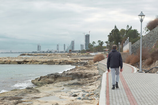 Lonely man walks along the sea on promenade, in the background skyscraper while built - Powered by Adobe