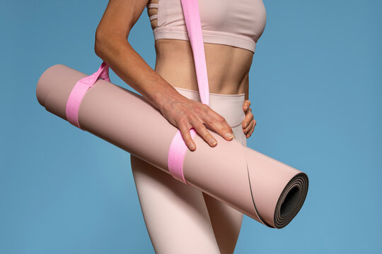 Close up of a woman carrying a pink yoga mat against a blue background - Powered by Adobe