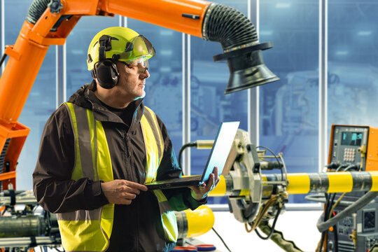 Man working in carpentry shop. Industrialist with laptop in yellow uniform. Contractor modern carpentry shop. Industrial equipment. Man industrialist in helmet with headphones and glasses - Powered by Adobe