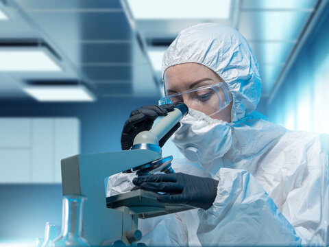Woman lab technician using microscope. Scientist studying dangerous bacteria. Lab technician in bacteriology lab. Scientists in white protective suit. Microbiologist with microscope focused on work