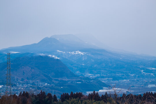 A serene view of layered mountains fading into mist, with snowy patches and a soft blue haze over the landscape.