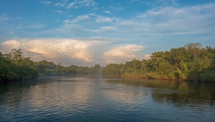 Obraz premium Scenic river flows serenely beneath a vibrant sky with fluffy clouds at golden hour for peaceful nature scenes