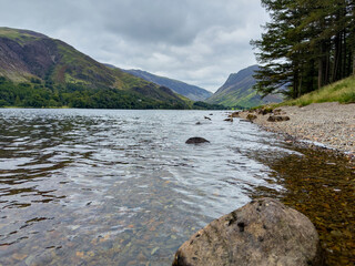 Calm reflective lake with mountain backdrop and rocky shoreline in scenic landscape.