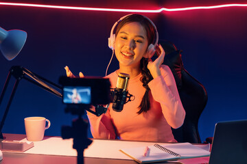 Fototapeta premium Host channel of creative broadcast listening the music on social media with listeners in positive podcast, wearing pastel color headphones, using mic radio record by camera at neon studio. Stratagem.