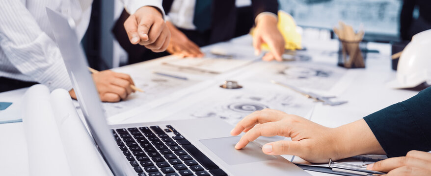 A collaborative team meeting taking place in a modern office where engineers and designers strategize over documents and a laptop, fostering creativity and teamwork. SACTR