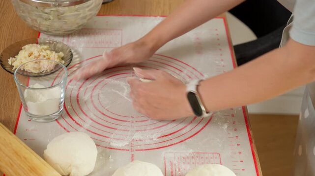 A woman carefully shapes portioned dough into smooth, round balls. It's a key part of a homemade recipe for making delicious, equally-sized piroshki or savory pies.