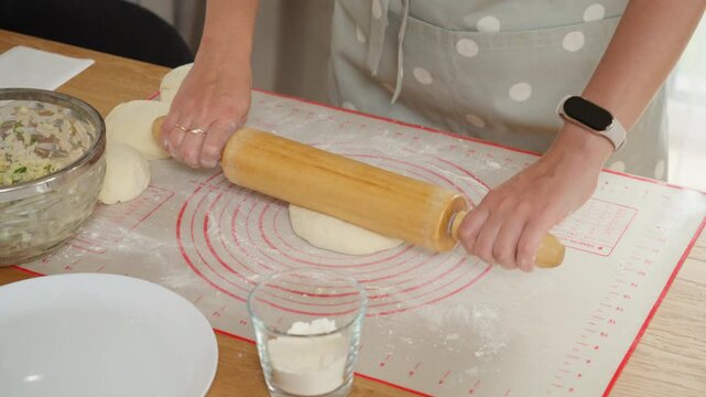 A woman carefully rolls out a sealed dough ball with a cheese and ham filling inside. This is the traditional method for making Georgian khachapuri or Ossetian pies.
