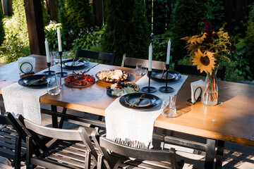 Outdoor Dinner Party Setting with Black Plates, Candles, Sunflower Arrangement and Wooden Table in Natural Garden Light