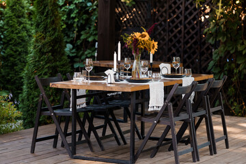 Outdoor Dining Setup with Wooden Table, Black Chairs, and Sunflower Centerpiece in Lush Garden Setting for Stylish Summer Events
