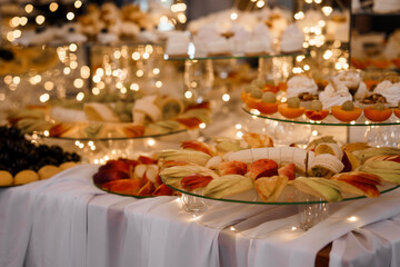 Festive Dessert Buffet with Fruits, Pastries, and Sparkling Lights: Elegant Wedding or Event Catering Table Display in Warm Tones