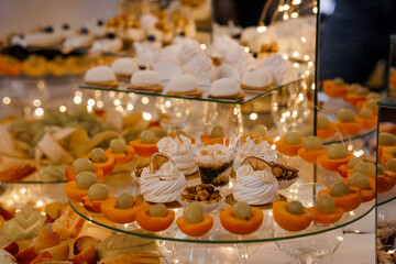 Elegant Dessert Spread at Wedding Reception: Tiered Cakes, Fruit, Pastries, Warm Lighting, Orange Accents, Festive Celebration, Close-Up View