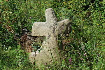 Ancient stone cross. Grass around the stone cross. The cross is carved from stone.