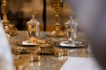 Orthodox Christian Holy Communion Vessels and Chalices with Crosses on Alter Cloth in Golden Church Interior.