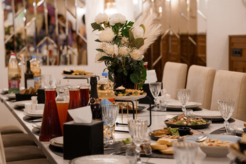 Elegant Dinner Party Setup with White Floral Arrangement, Drinks, Appetizers, and Table Setting in a Modern Interior.