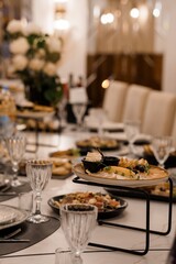 Elegant Wedding Table Setting with Appetizers and Crystal Glassware. Luxurious Reception Dinner with White Flowers, Marble Table, and Warm Lighting