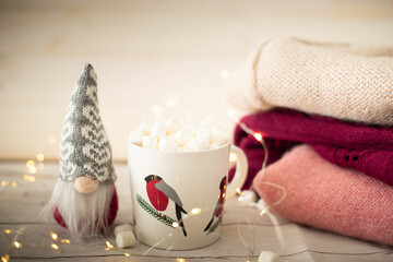 Christmas still life with robin cup filled with chocolate and marshmallows, gnome doll and string lights. Festive, cozy  background with copy space.