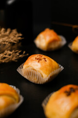 Close up of single banana–chocolate bolen in a cup liner against dark background; glossy golden crust with flaky puff layers. Perfect for bakery branding, menus, recipe visuals, and ads.