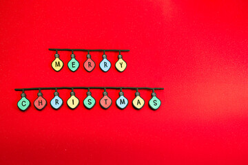 Christmas garland made of colored light bulbs spelling out “Merry Christmas” on a red background. Wooden letters. Space for text