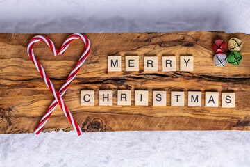 Merry Christmas message with candy canes and jingle bells, on wood and white background