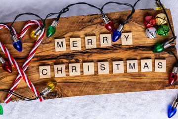 Merry Christmas on a holiday greeting with candy canes and festive lights. Letters on wooden tiles