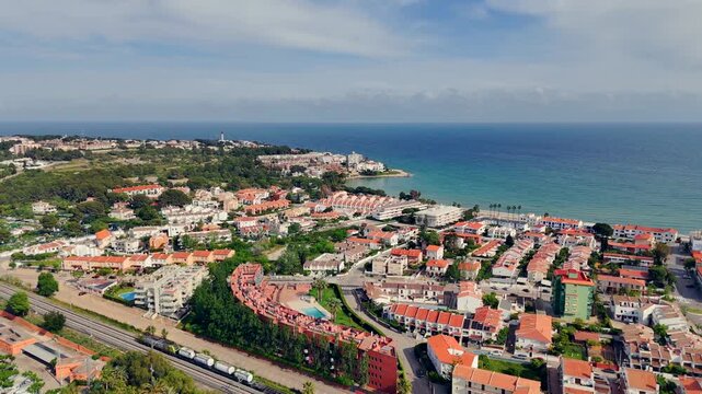 Aerial drone video of freight train traveling along train tracks through a small Spanish town along the coast. Filmed in Altafulla, Spain.
