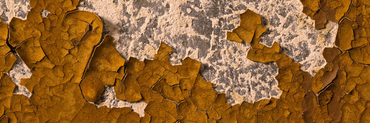 Peeling paint on the wall. Panorama of a concrete wall with old cracked flaking paint. Weathered rough painted surface with patterns of cracks and peeling. Wide panoramic grunge texture for background